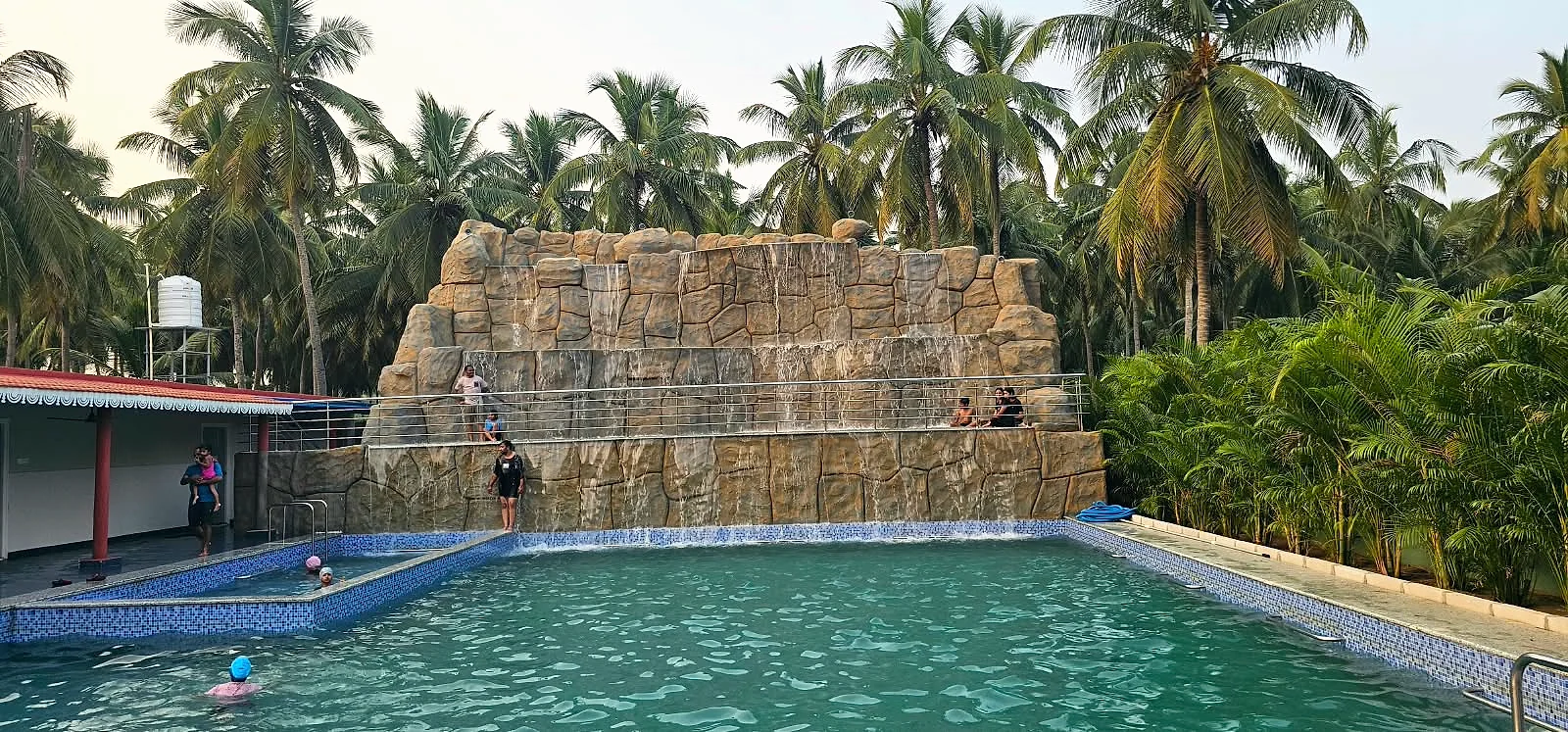Children enjoying the resort swimming pool beneath the waterfall and palm trees