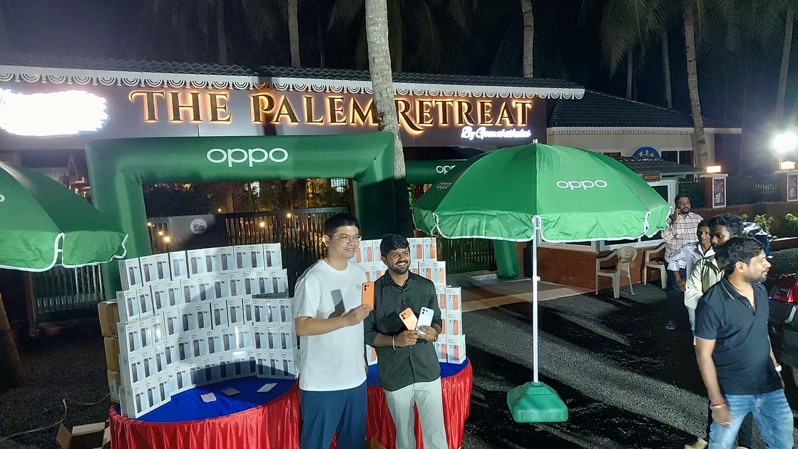 Two attendees posing with phones in front of the OPPO display and The Palem Retreat sign